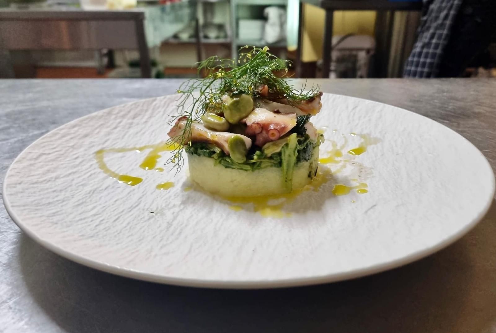 Antipasto gourmet con gamberi, verdure e salsa su un piatto bianco, servito in un ambiente da ristorante.