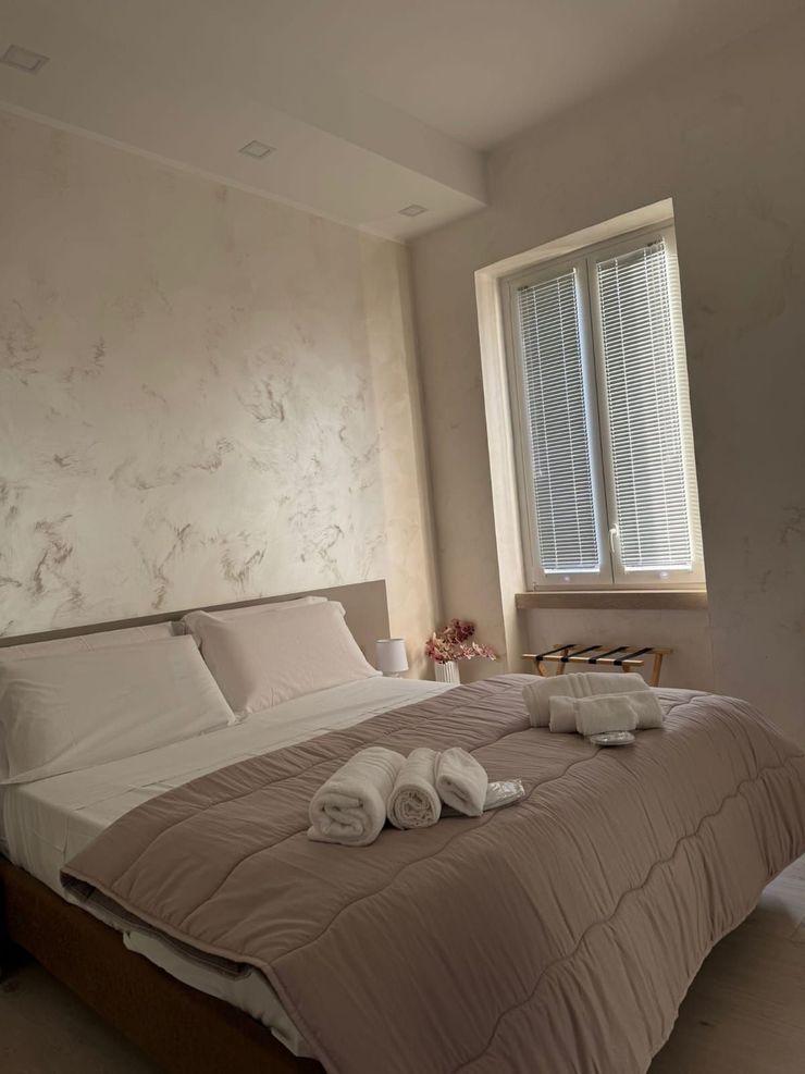 Letto ben rifatto con asciugamani piegati in una camera da letto luminosa accanto a una finestra con persiane.
