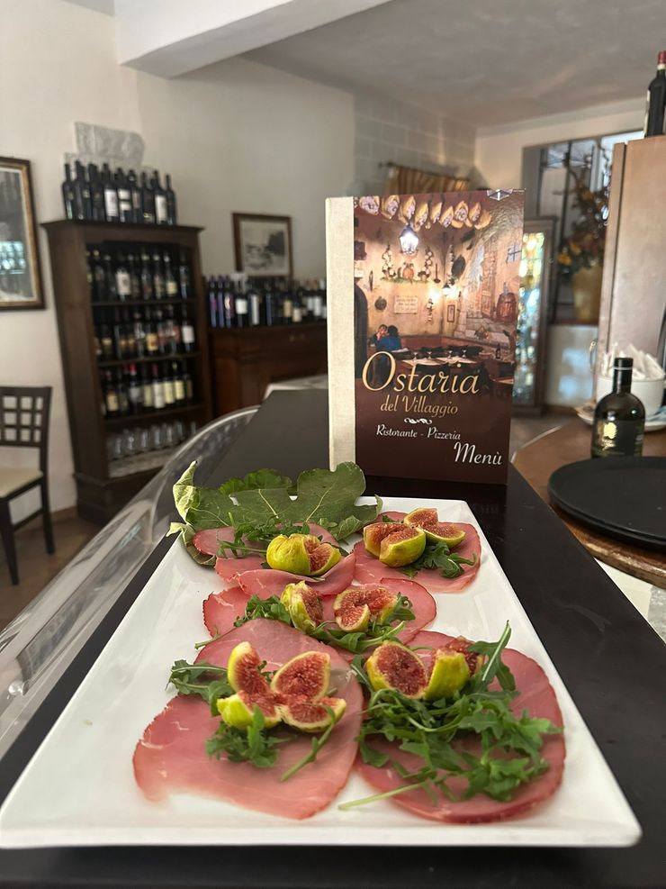 Antipasti a base di prosciutto e fichi serviti su un piatto bianco in un ambiente da ristorante.