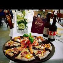 Una pizza su un tavolo con una bottiglia di vino e un menù del ristorante, in una sala da pranzo.