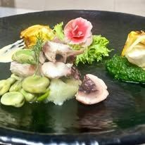 Sushi assortito e frutti di mare affettati disposti su un piatto nero con verdure e un fiore rosa commestibile.