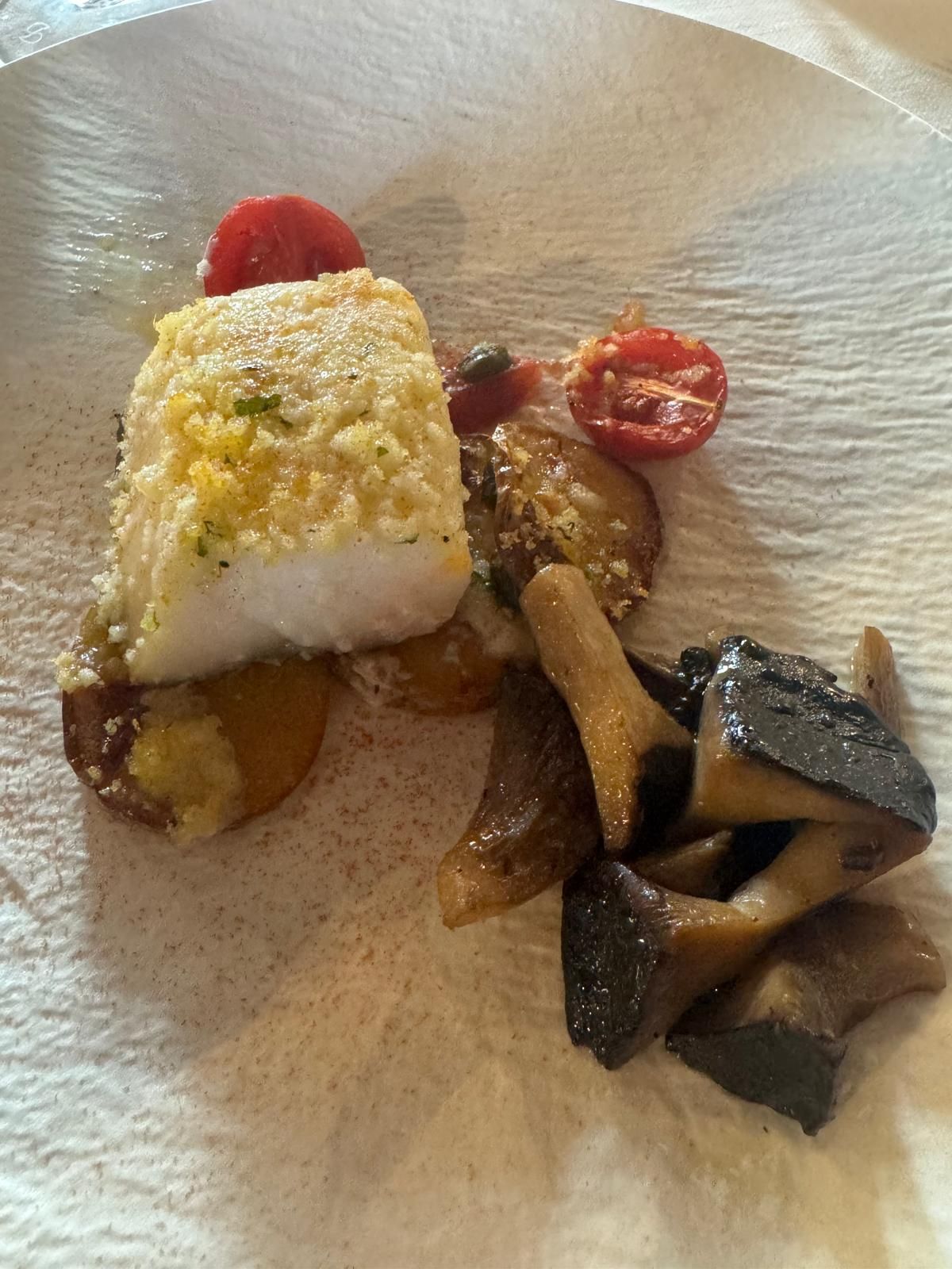 Piatto gourmet impiattato con pesce scottato, verdure arrostite e guarnizione rossa su un piatto bianco.