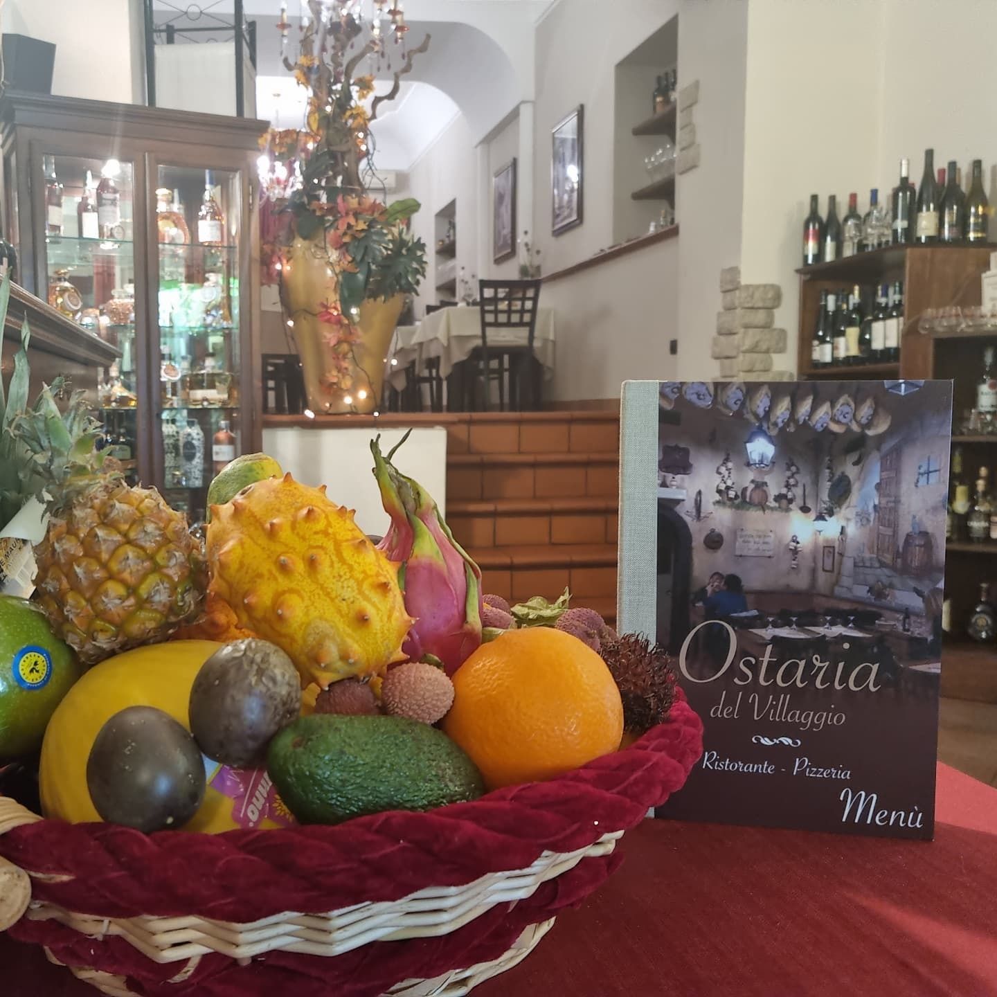 Un cesto di frutta nell'accogliente ingresso di un ristorante, accanto a un menù e a un espositore di vini.