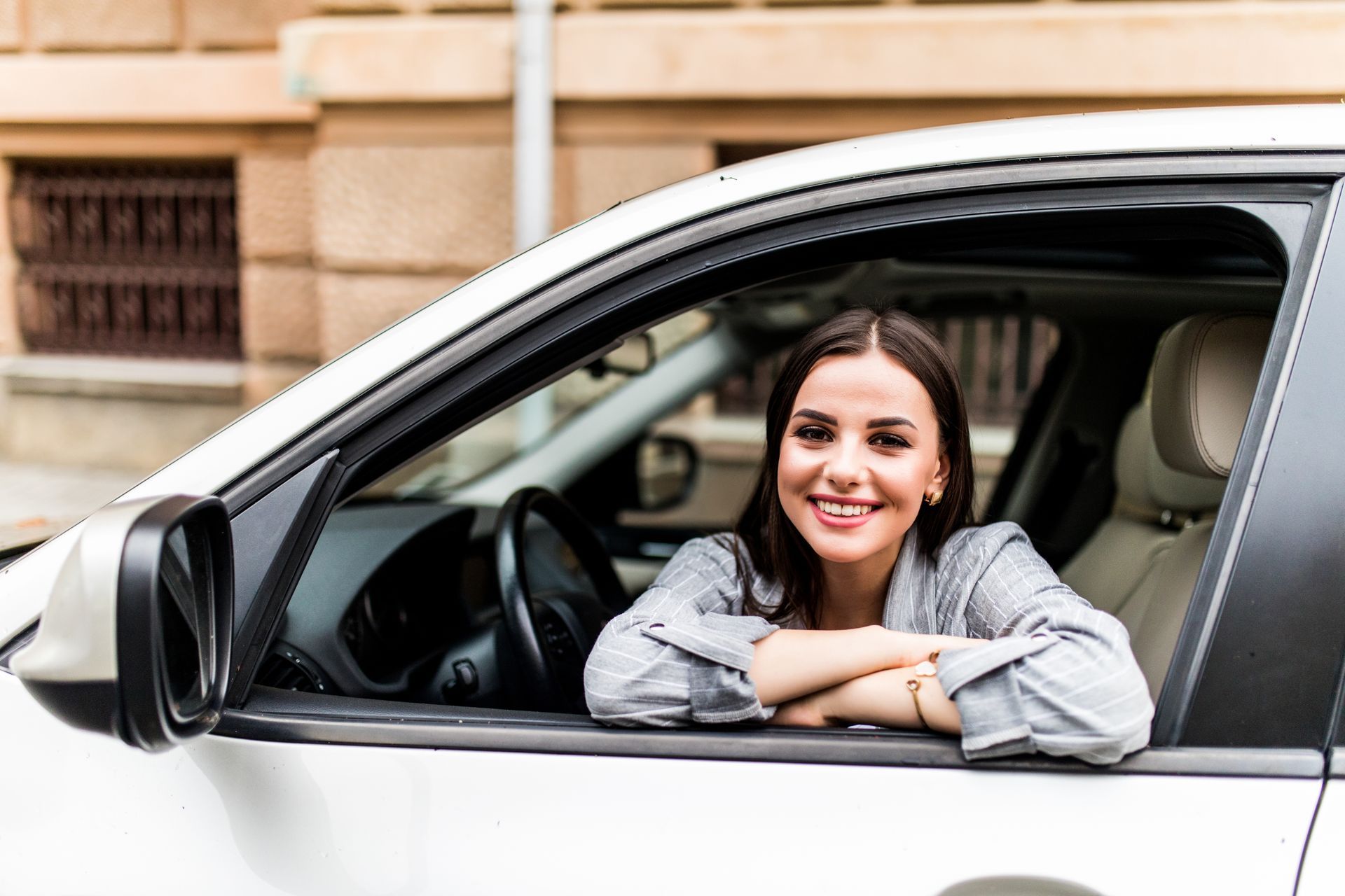A woman is sitting in a car with her arms crossed and smiling.