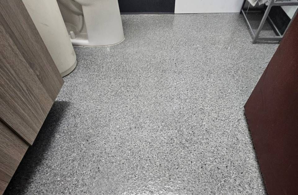 Empty speckled floor in a hallway with cabinets and a chair leg visible.