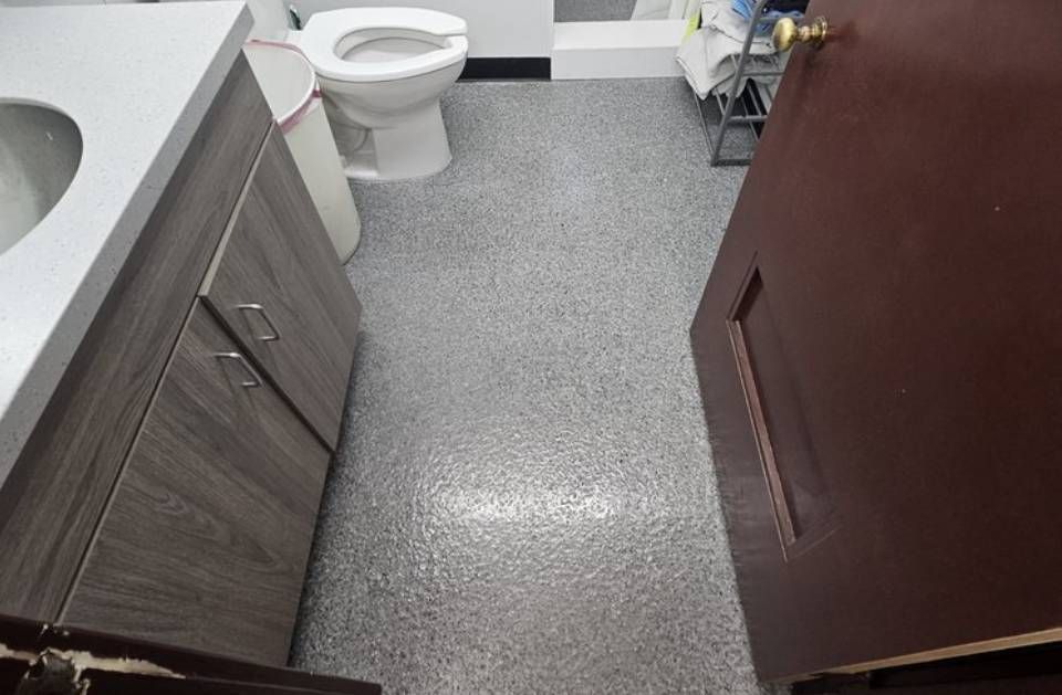 Small bathroom with toilet, sink cabinet, speckled floor, and a large brown cabinet or stall on the right.