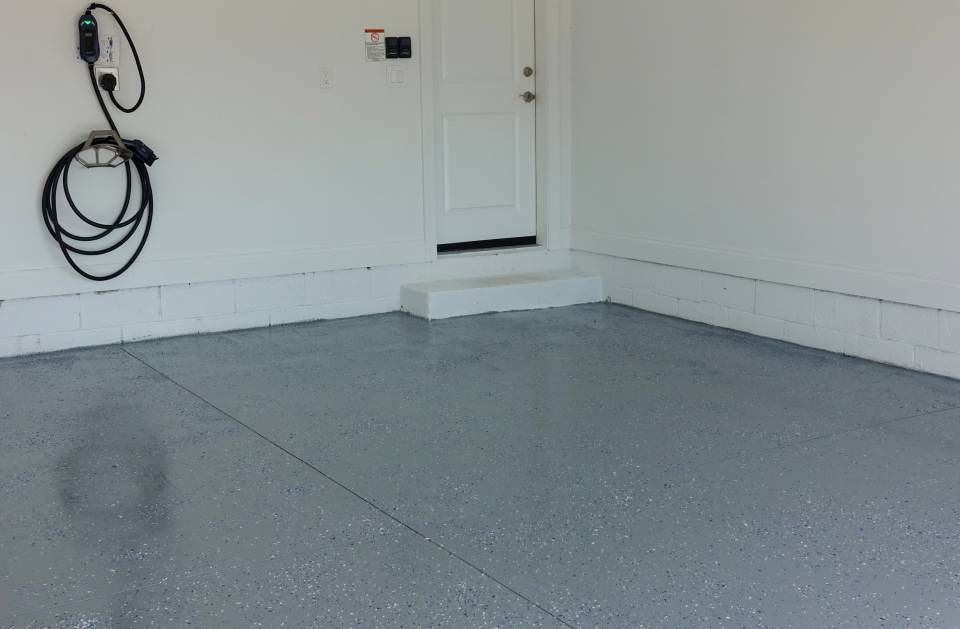 Empty white garage with a gray epoxy floor and a coiled wall hose.