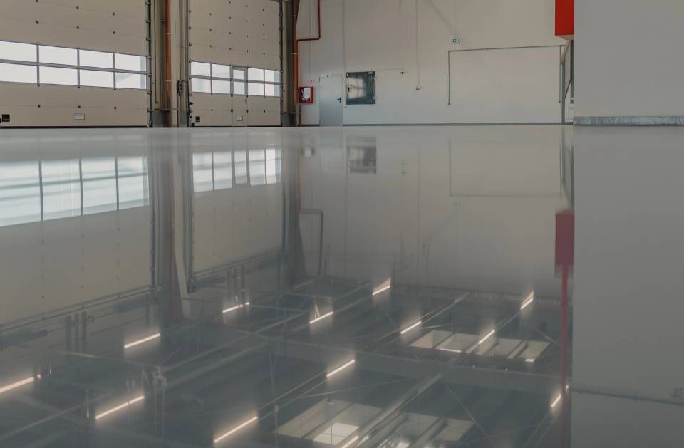 Glossy empty industrial floor reflecting overhead lights in a warehouse-like room