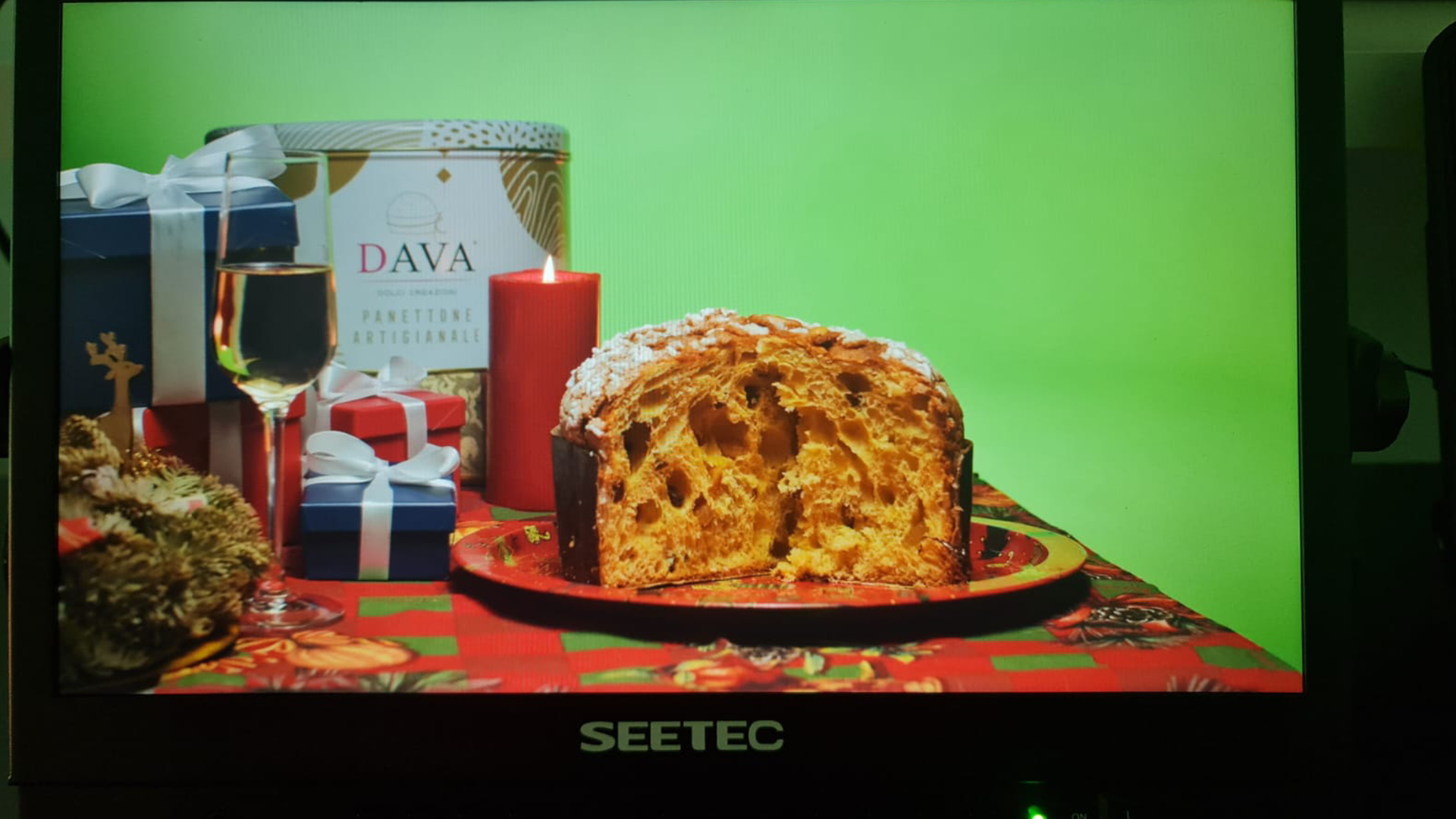 Panettone su una tavola festiva con regali, una candela e un bicchiere di champagne su uno sfondo verde.