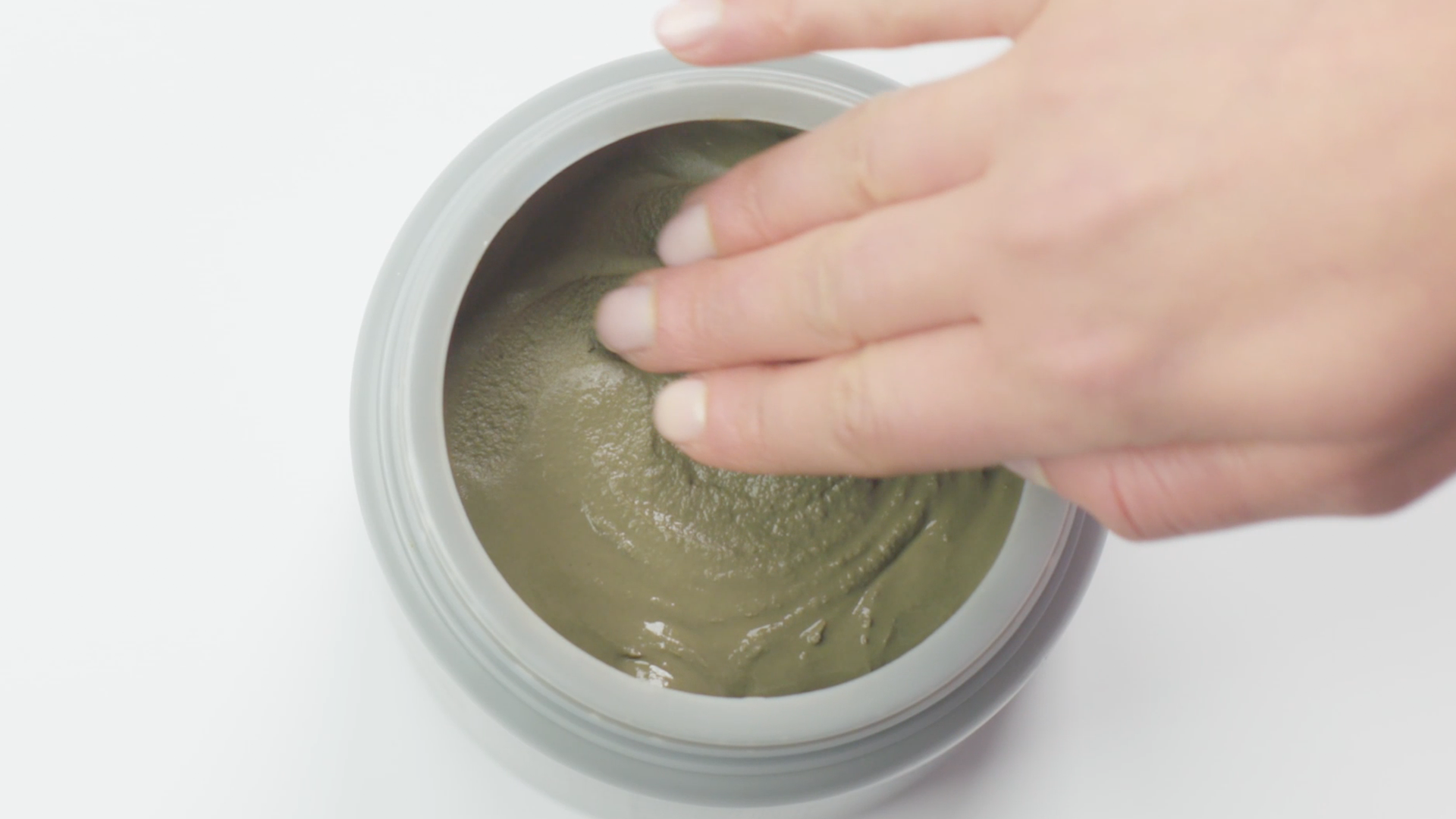 Hand touching a gray, creamy substance in a light gray jar.