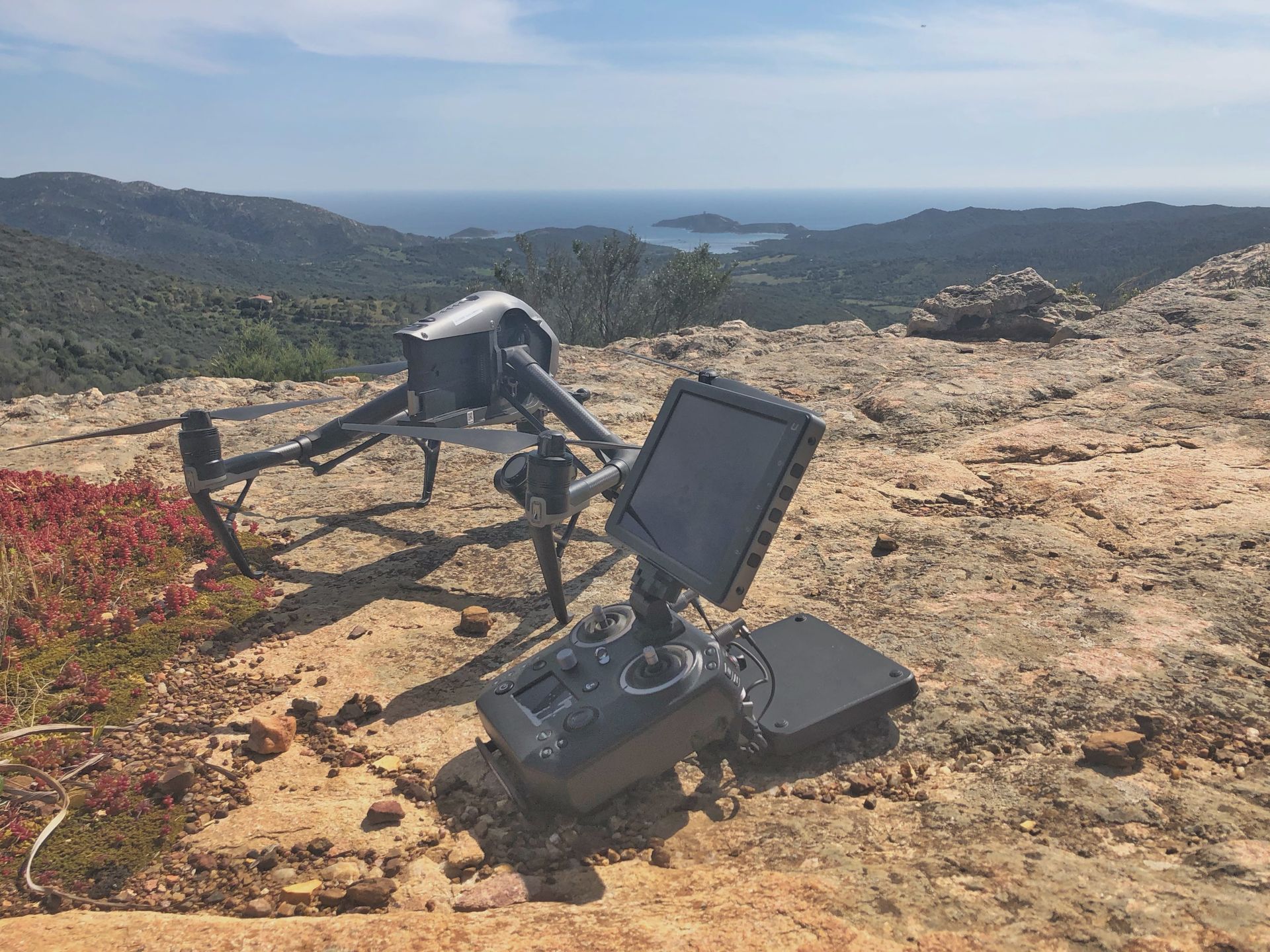 Drone and remote control on a hilltop overlooking a scenic view of ocean and hills.