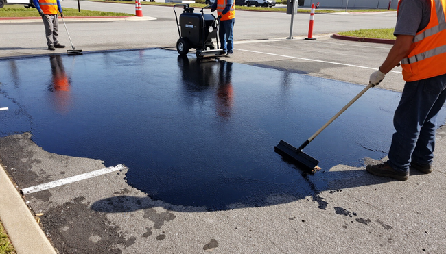 Worker applying black sealcoat across asphalt during sealcoating in Dallas, TX