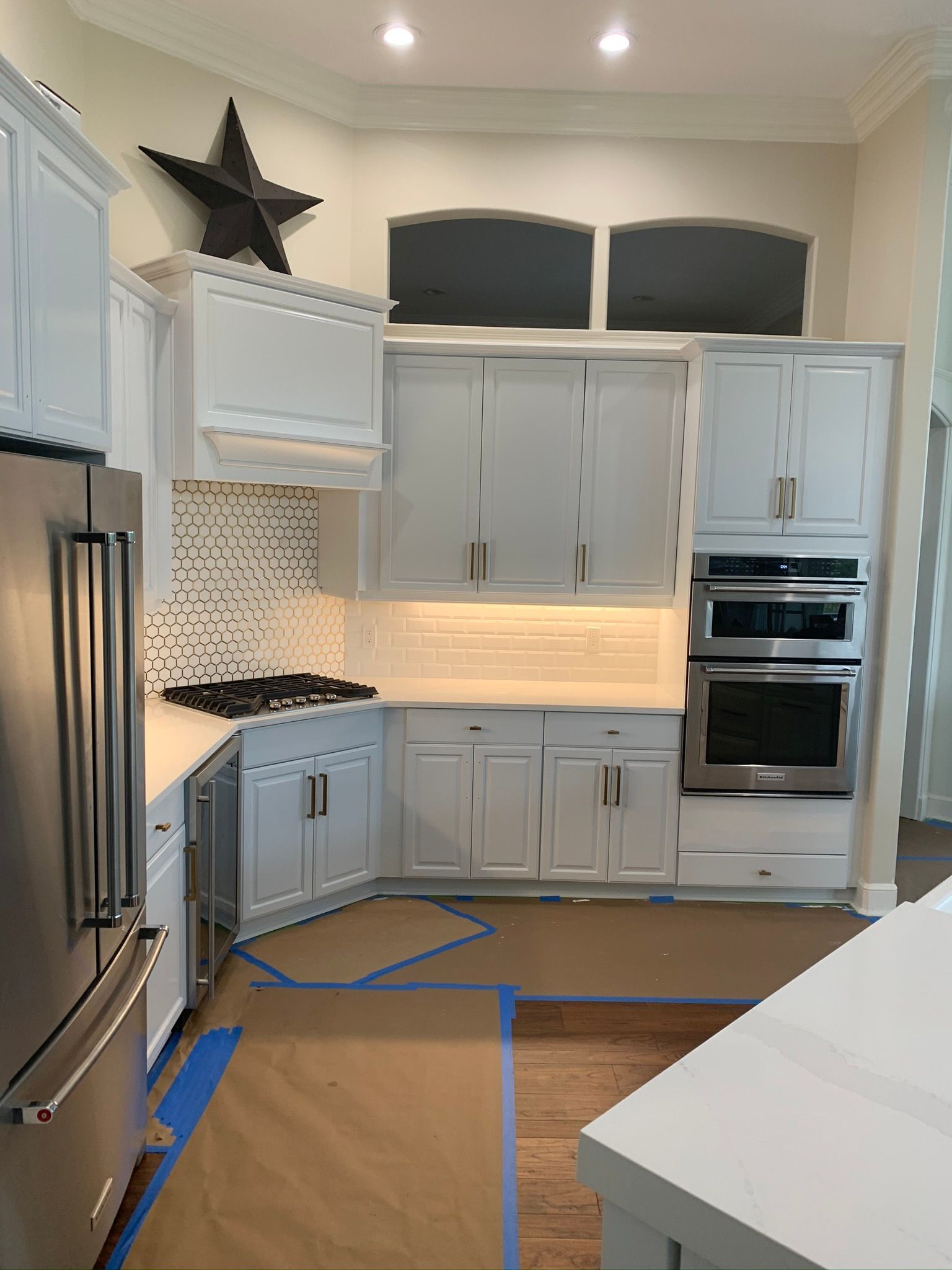 Modern white kitchen with gray cabinets, stainless appliances, and taped floor under renovation