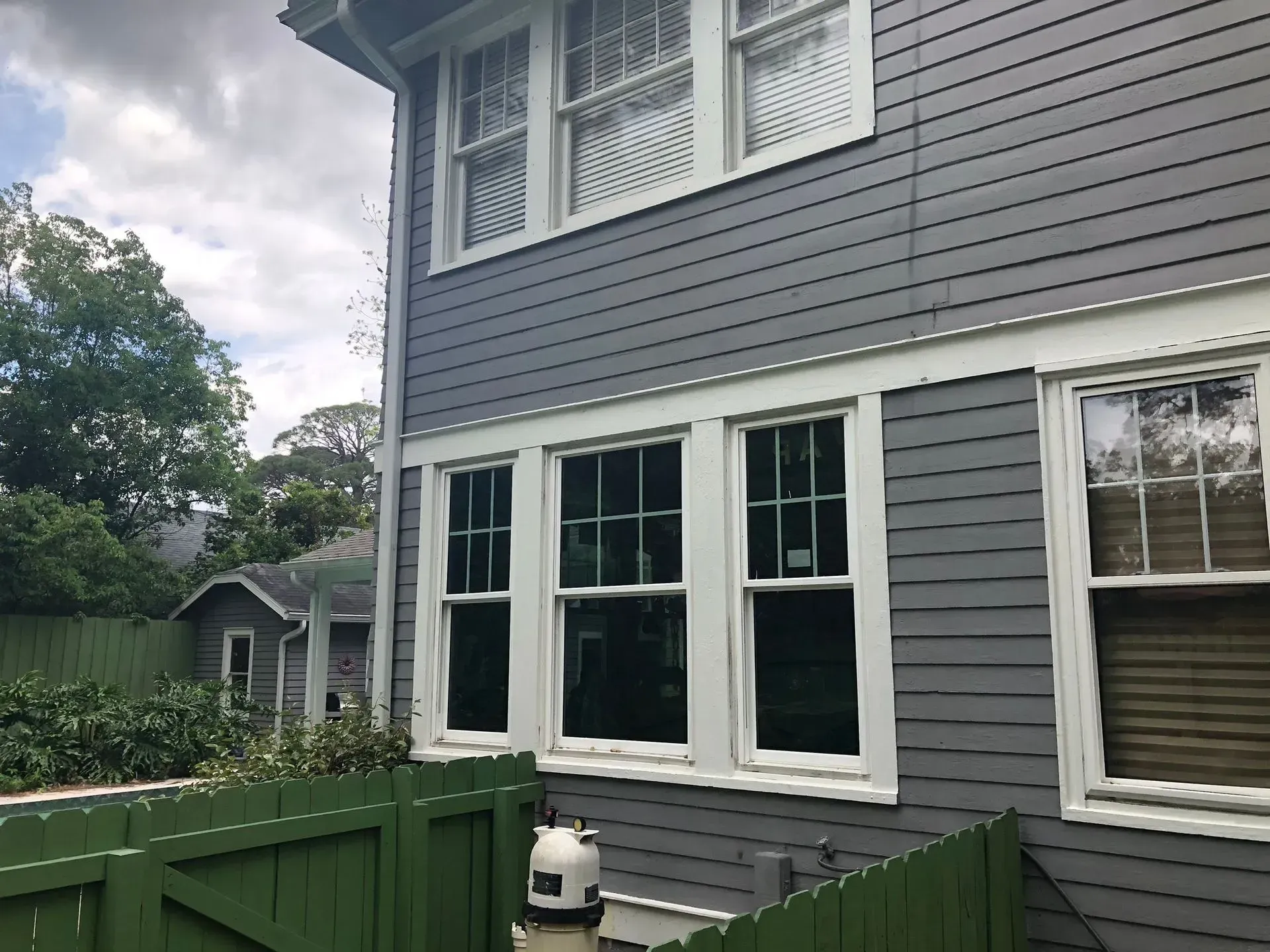 Gray house exterior with white-trimmed windows and green shrubs in front