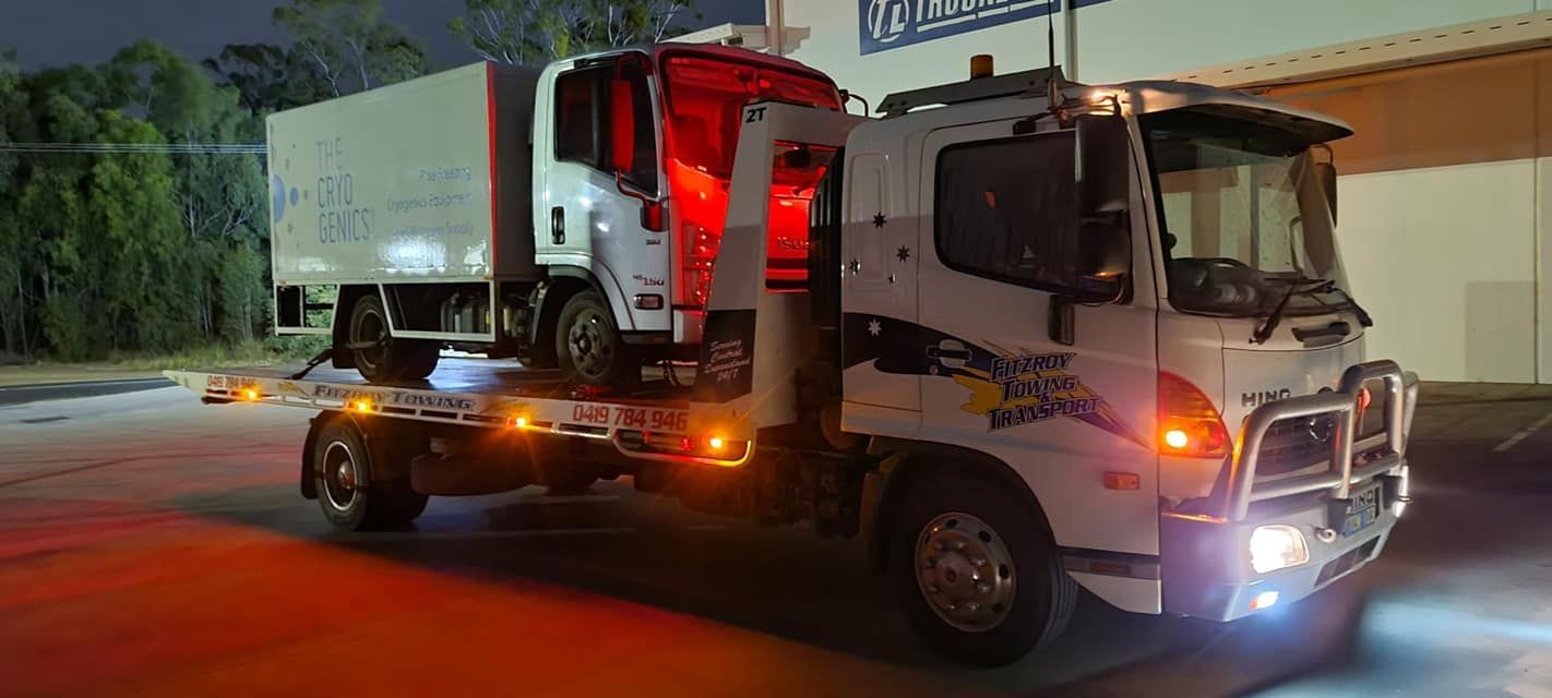 A White Tow Truck at Night Carrying Another Truck With Red Lights Illuminated — Fitzroy Towing & Transport in Yeppoon, QLD
