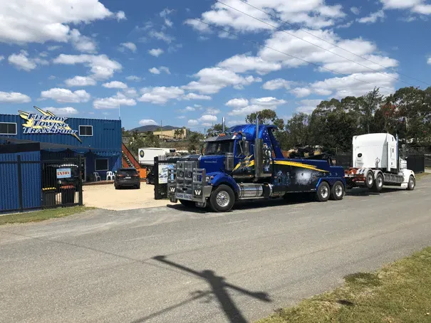 Blue Tow Truck Towing White Truck in Front of a Blue Building — Fitzroy Towing & Transport in Biloela, QLD