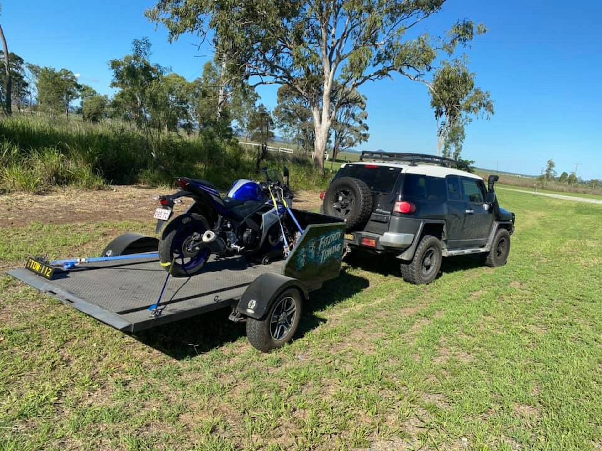 Black Suv Towing a Motorcycle on a Trailer in a Grassy Field on a Sunny Day — Fitzroy Towing & Transport in Biloela, QLD