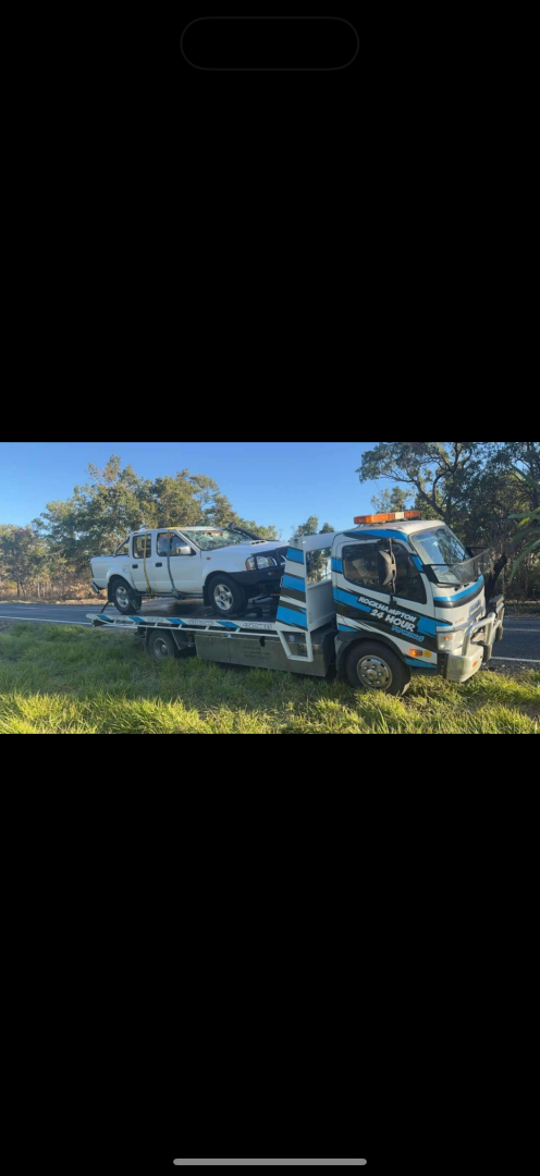 Tow truck carrying a white pickup truck on a grassy roadside.— Fitzroy Towing & Transport in Parkhurst, QLD