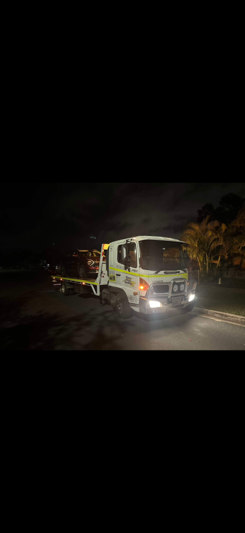 A tow truck with headlights on sits on a dark road at night.— Fitzroy Towing & Transport in Parkhurst, QLD