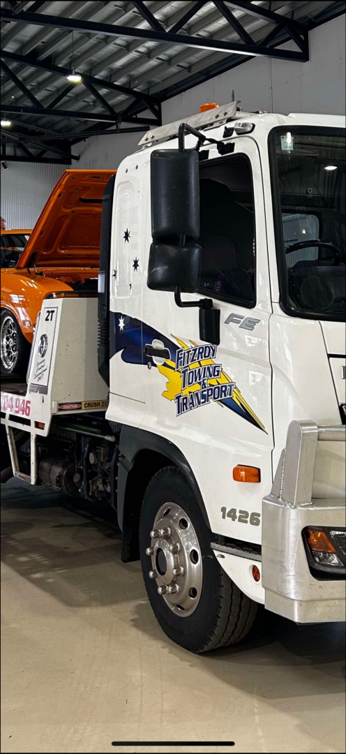 White tow truck with orange car on flatbed.  Blue and yellow logo on truck's side.— Fitzroy Towing & Transport in Parkhurst, QLD