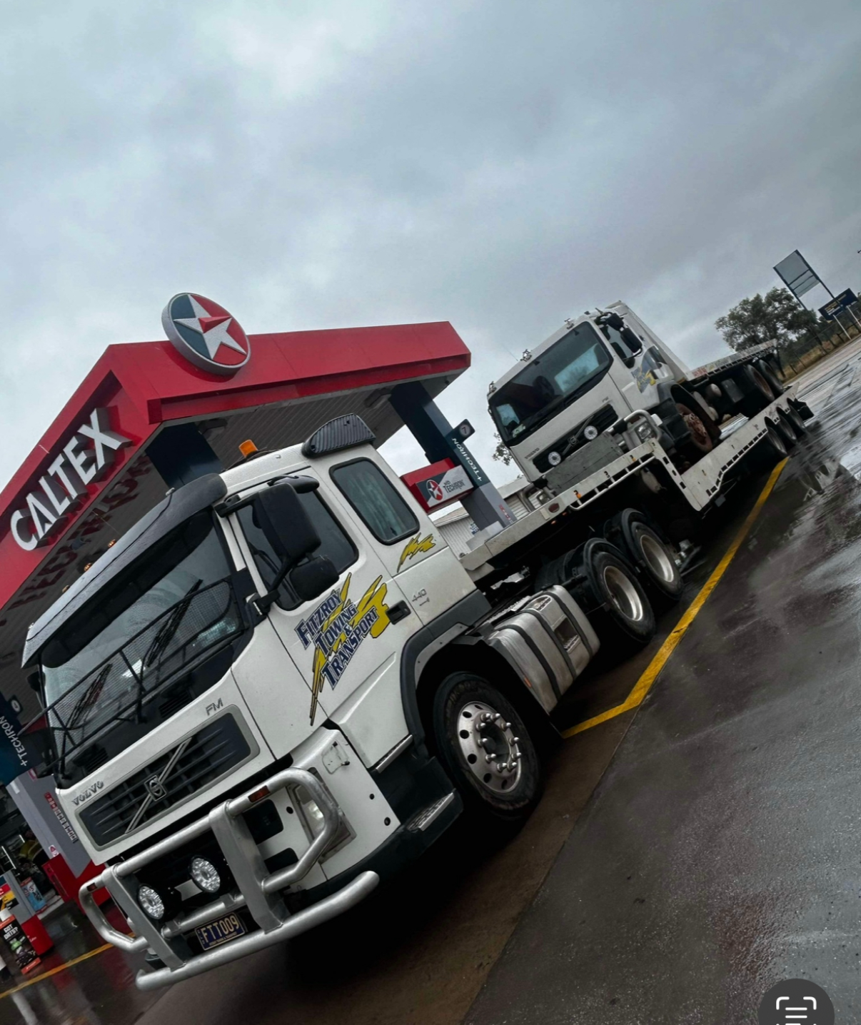White Semi-truck With a Tilt Trailer on Grass, Under a Blue Sky — Fitzroy Towing & Transport in Parkhurst, QLD