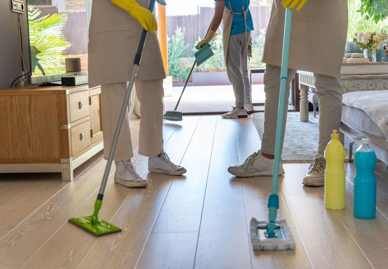 People mopping a bright kitchen floor with green, blue, and teal cleaning tools and bottles