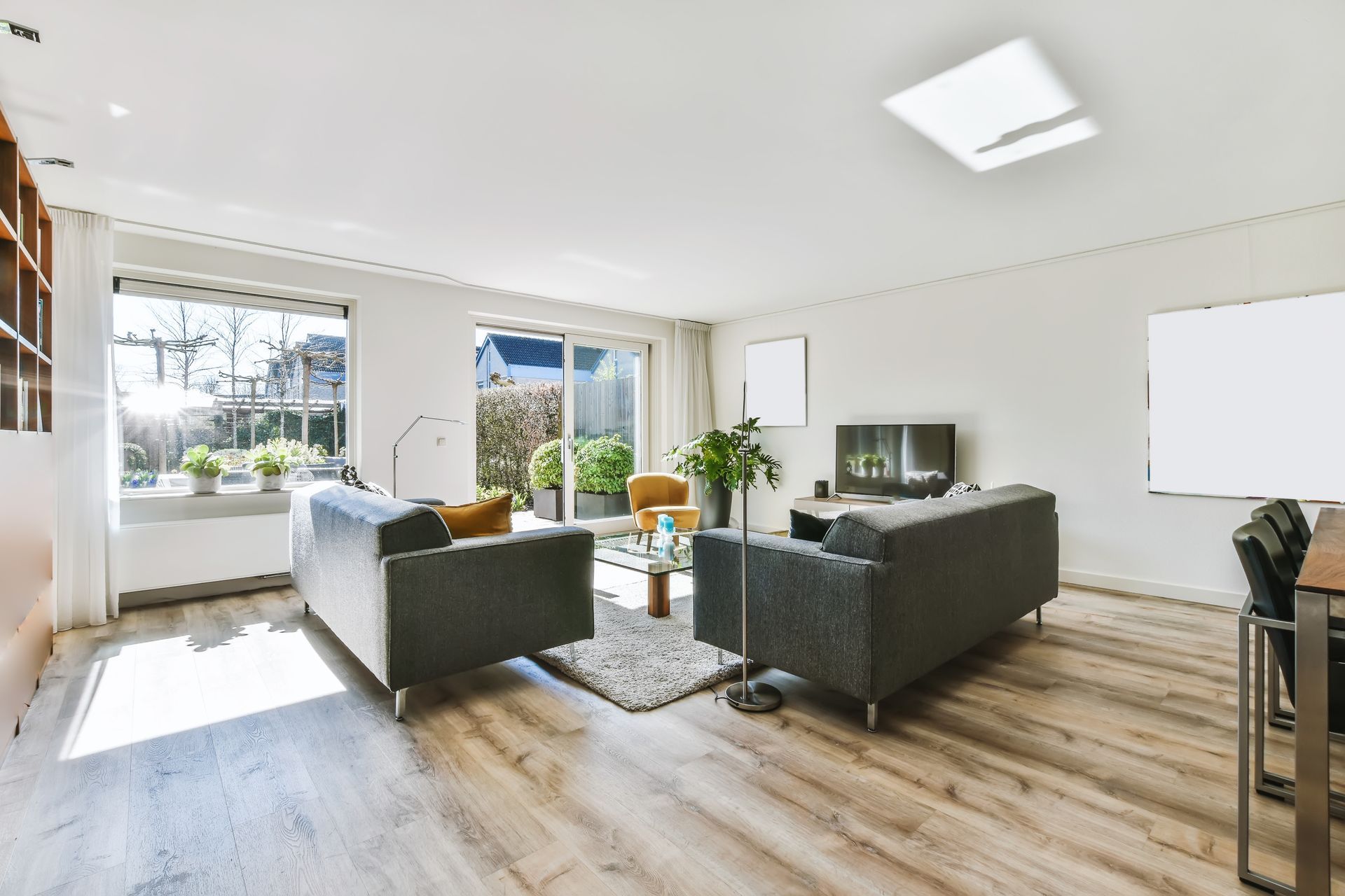 Bright modern living room with gray sofas, large windows, wood floors, and a wall-mounted TV