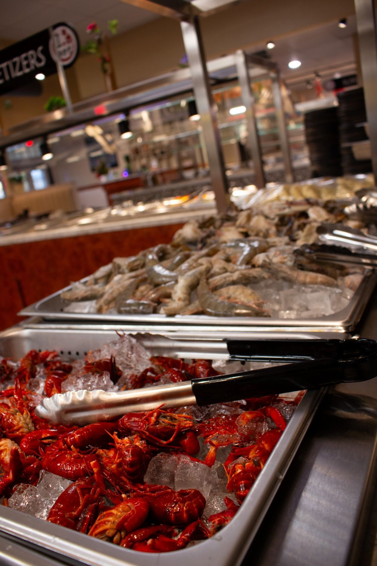 Tray of red cooked crawfish with metal tongs at a buffet counter