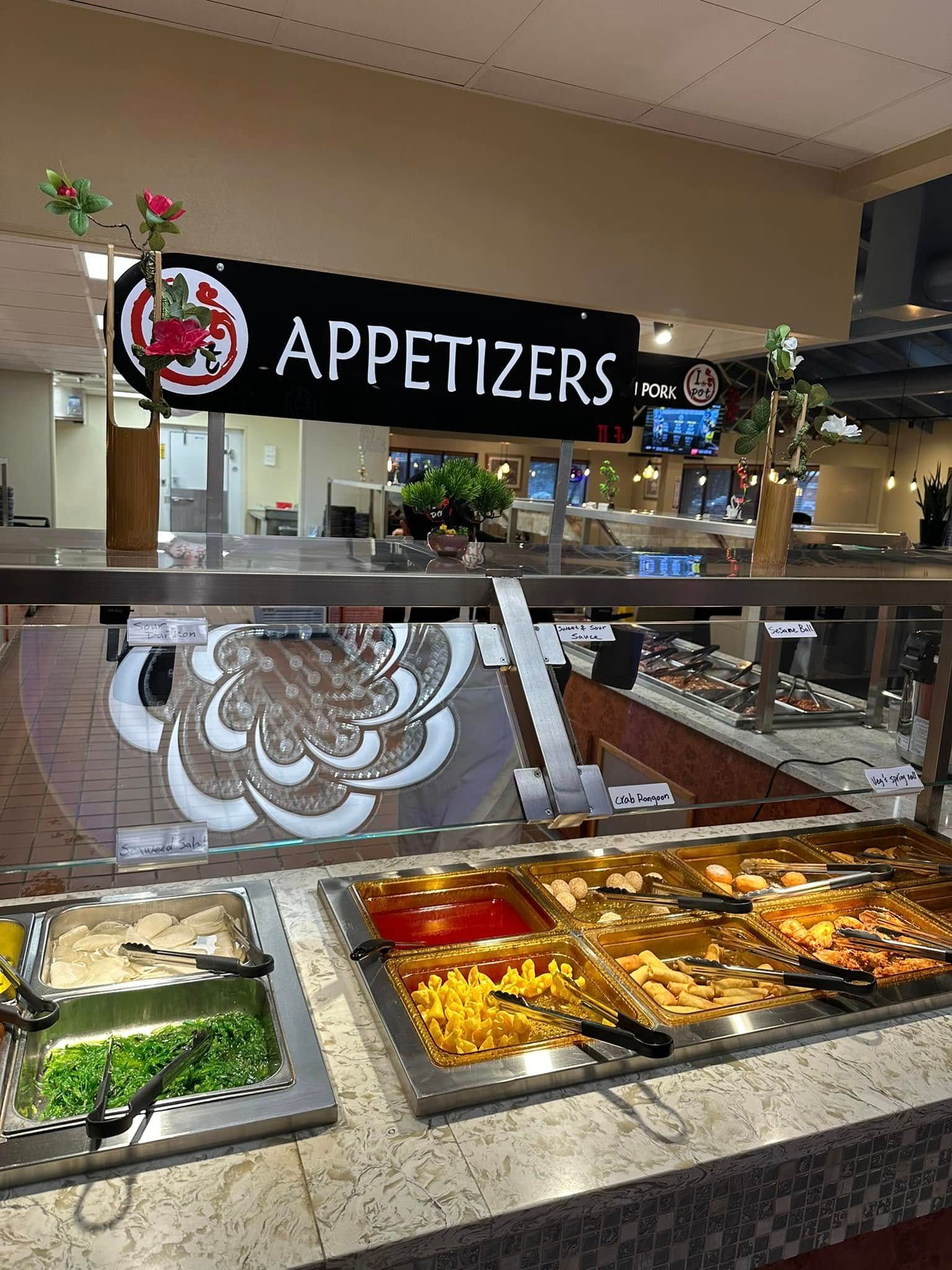 Buffet counter labeled “APPETIZERS” with assorted trays of hot and cold food under warm lights