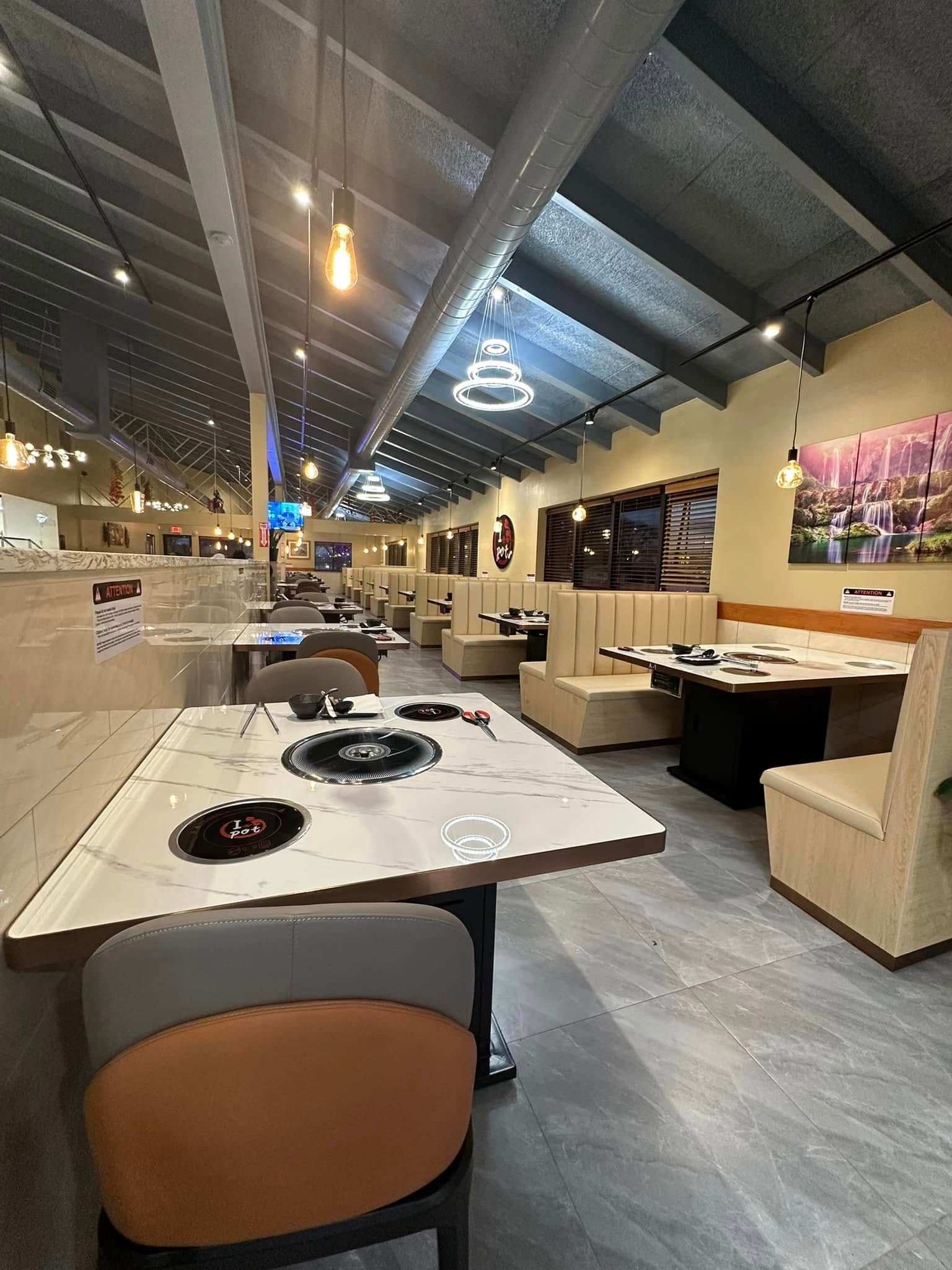 Empty modern restaurant with tables, booths, pendant lights, and a high ceiling