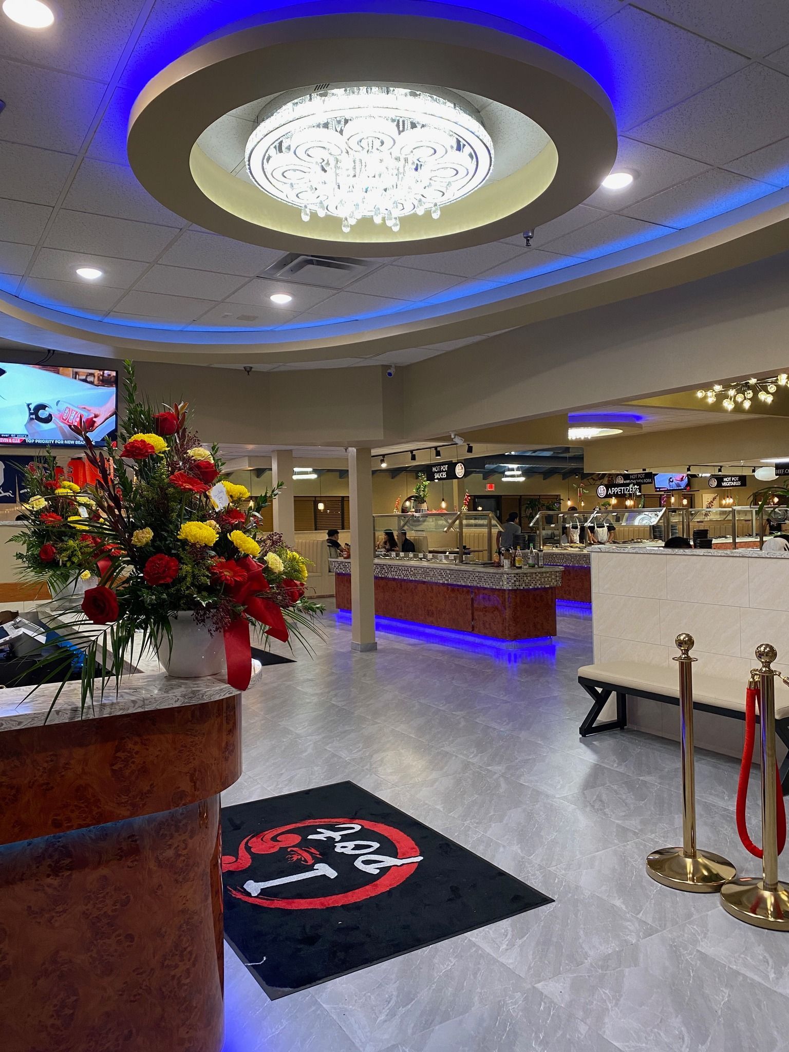 Modern hotel lobby with blue-lit ceiling, floral display, reception counter, and velvet stanchions