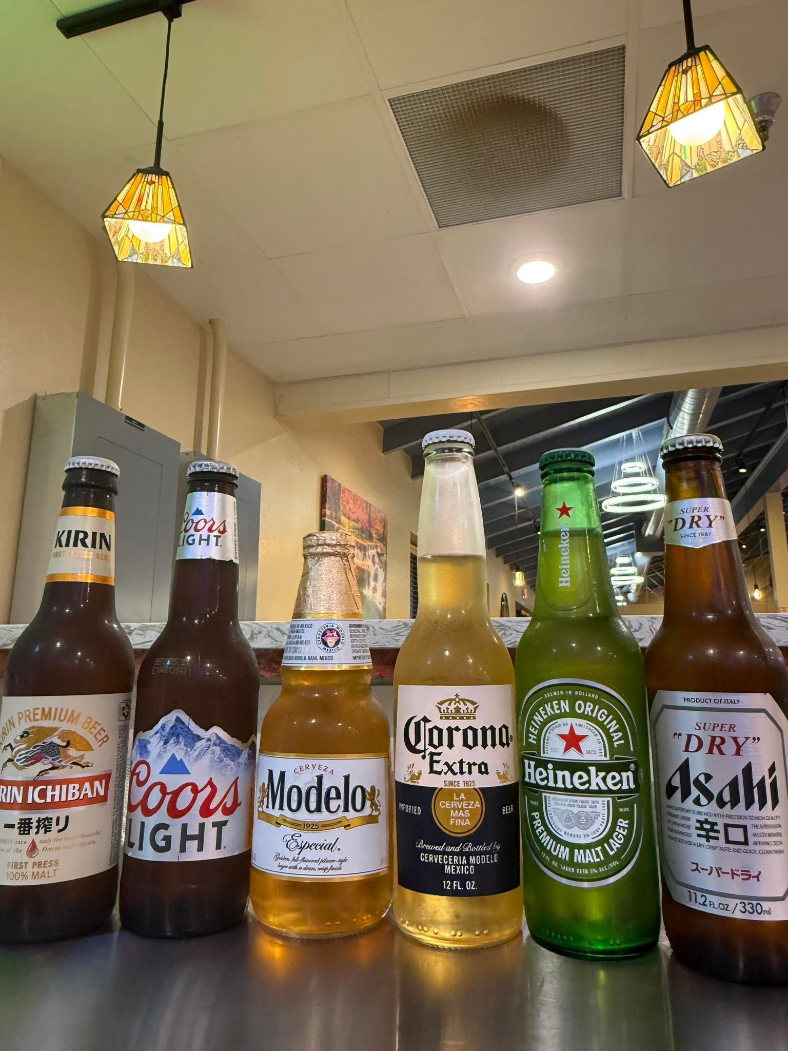 Assorted beer bottles lined up on a table under indoor ceiling lights