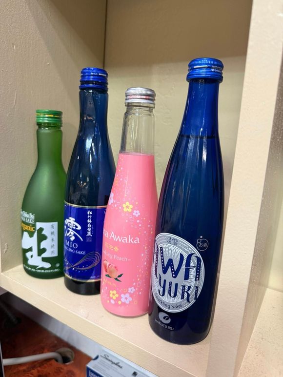 Four colorful glass bottles standing on a shelf, including blue, pink, and green bottles with labels.