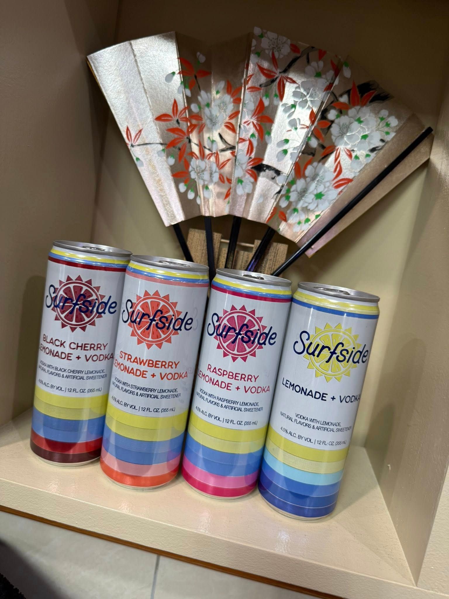 Five colorful cylindrical packages on a shelf beneath a decorative floral folding fan