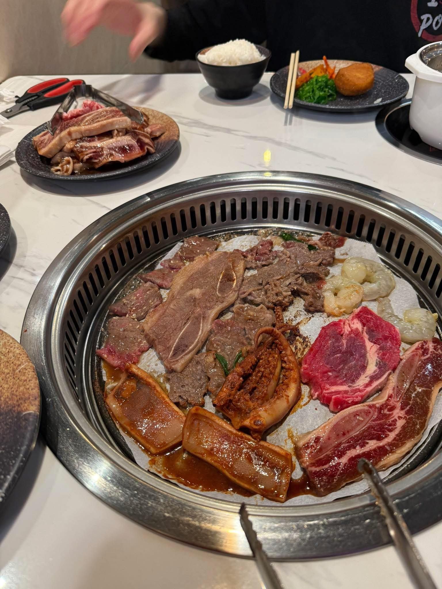 Korean barbecue grill with assorted raw and cooked meats sizzling at a restaurant table