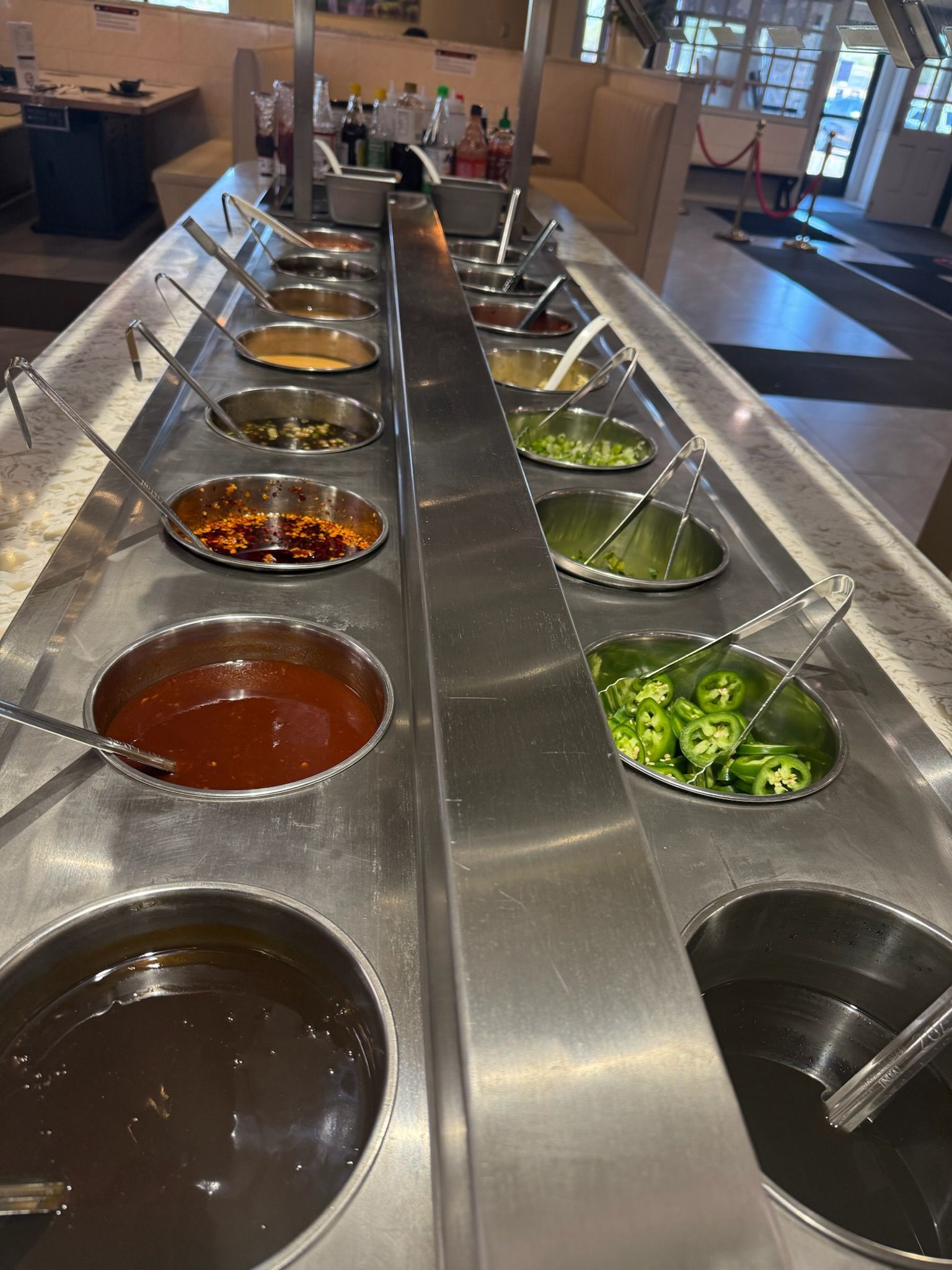 Buffet-style salad bar with metal trays of dressings and chopped vegetables under a glass sneeze guard