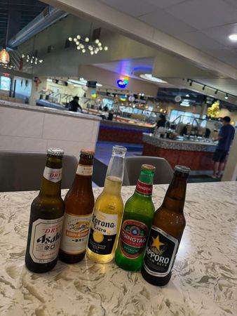 Four beer bottles on a counter in a restaurant/bar with a lit bar in the background