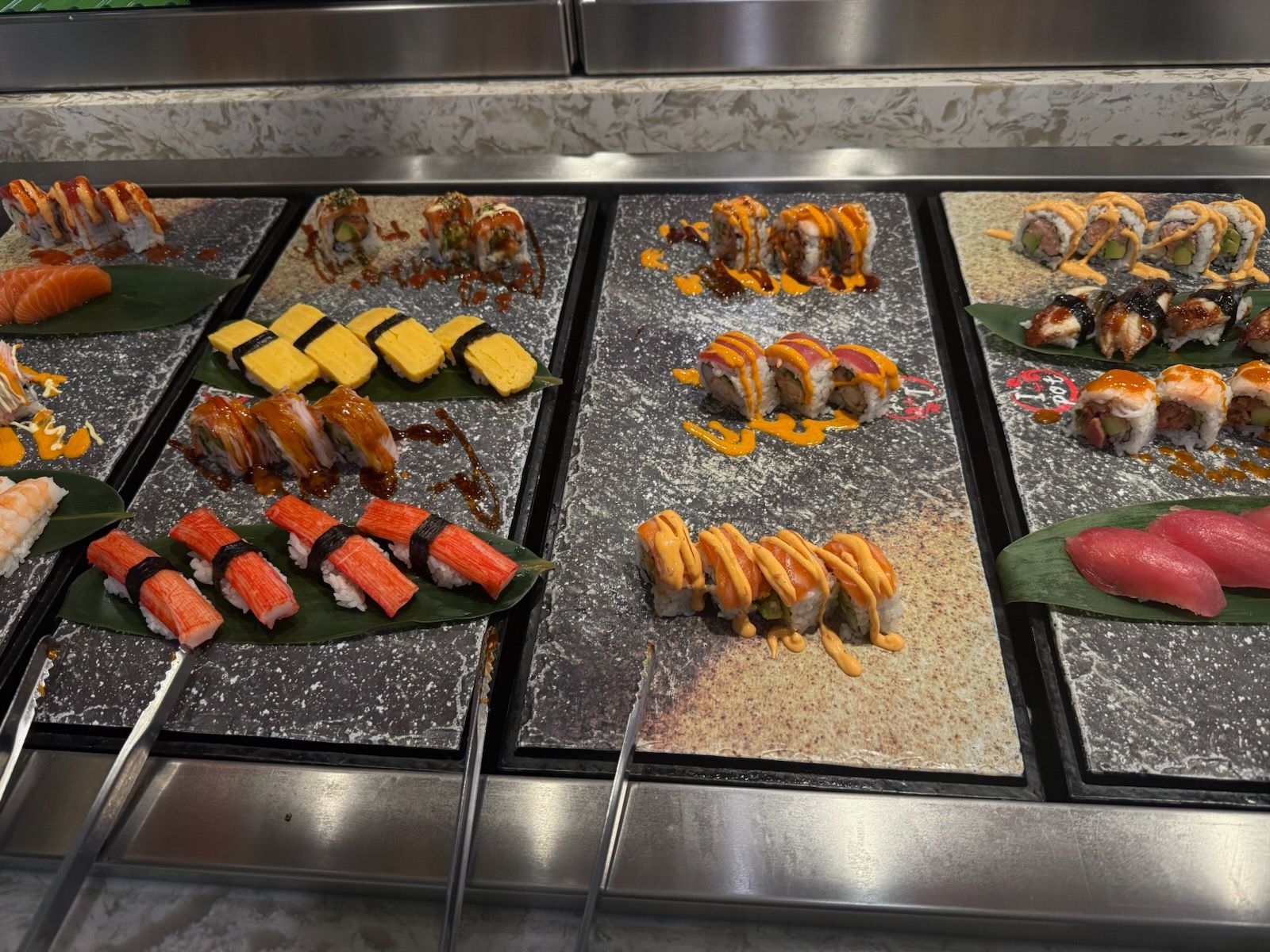 Sushi rolls and nigiri displayed on trays at a restaurant counter.
