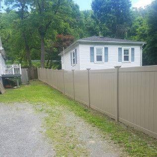 Tan vinyl fence surrounding a white house with blue shutters and a gravel driveway.