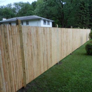 Wooden picket fence surrounding a grassy yard next to a two-story white house.