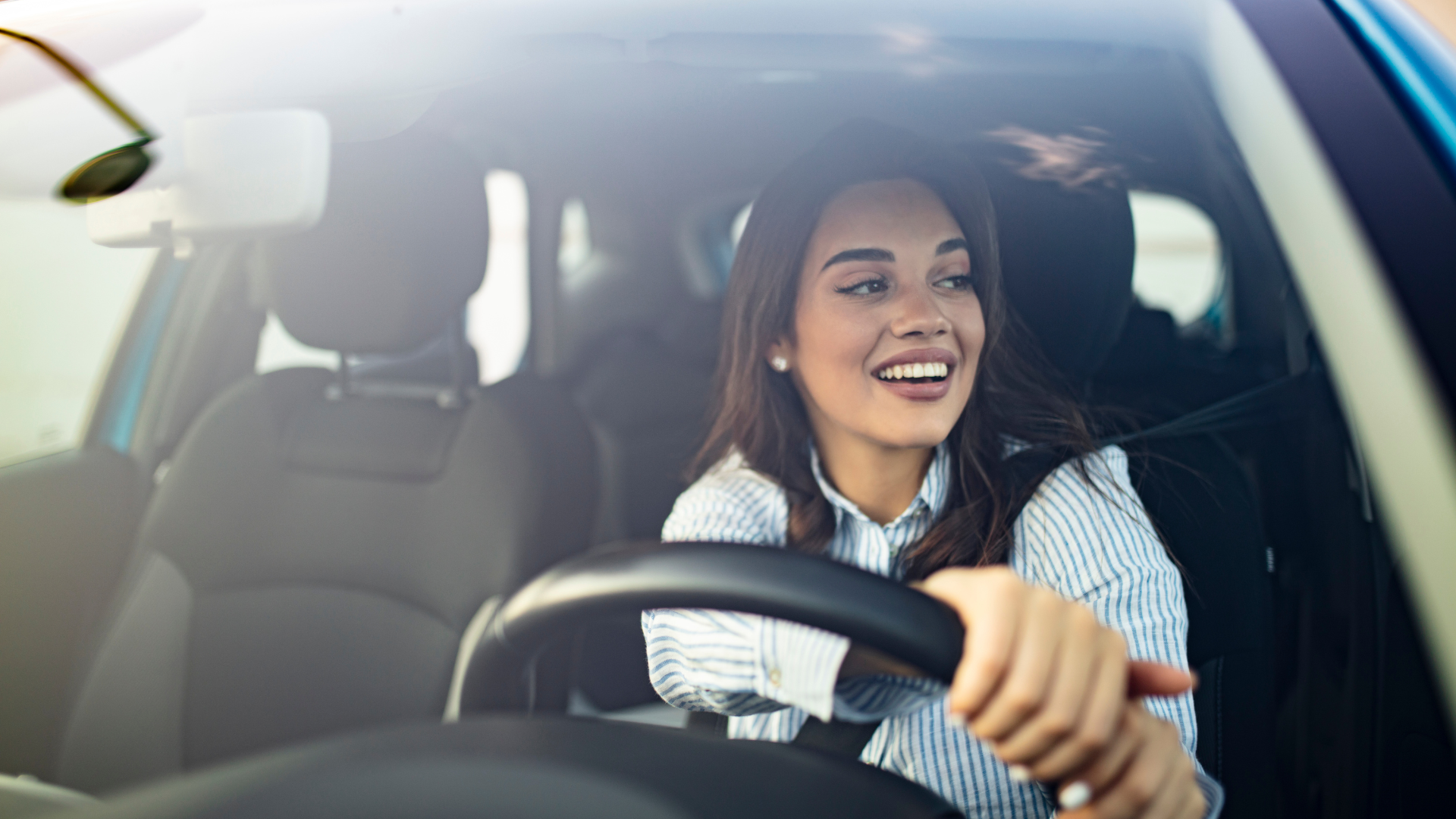 A woman is driving a car and smiling.