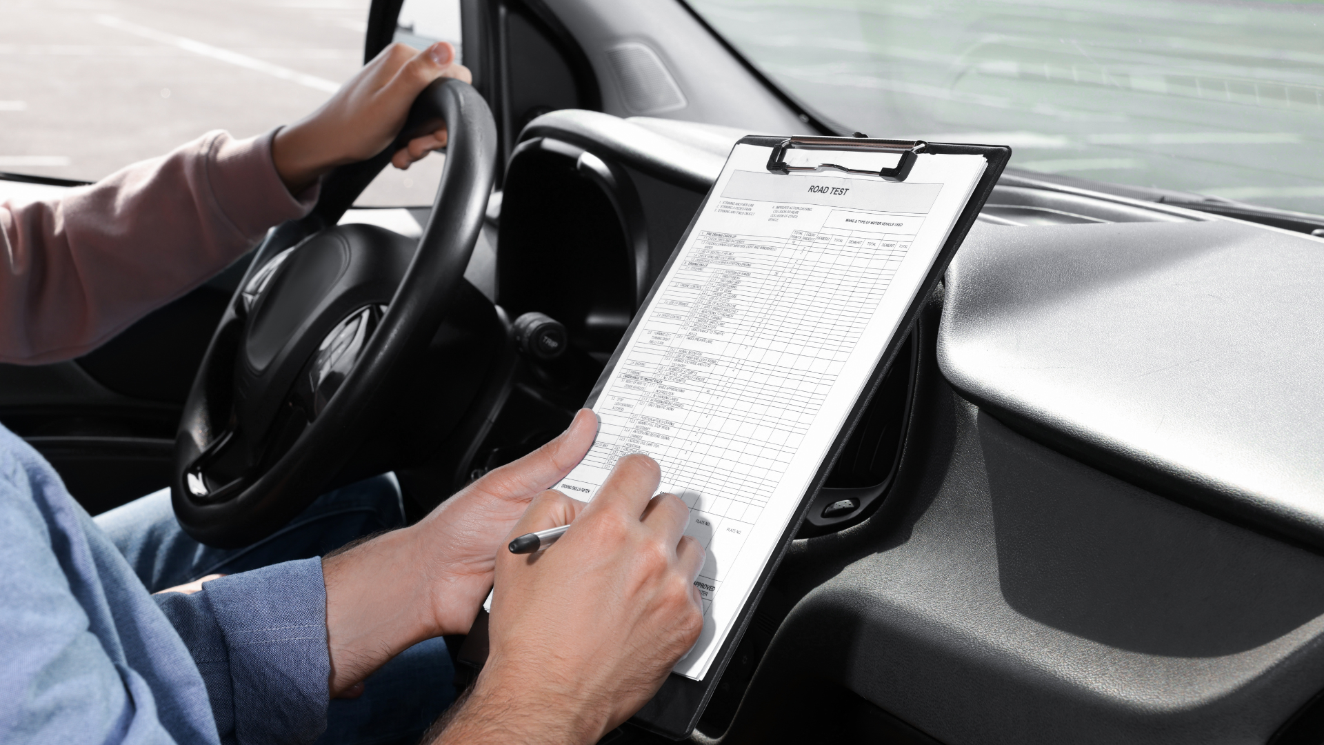 A man is sitting in a car writing on a clipboard.