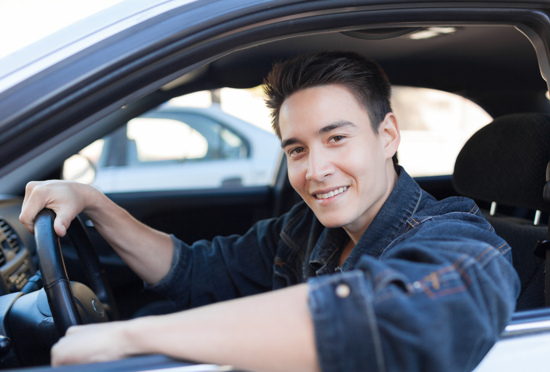A young man is sitting in a car and smiling.