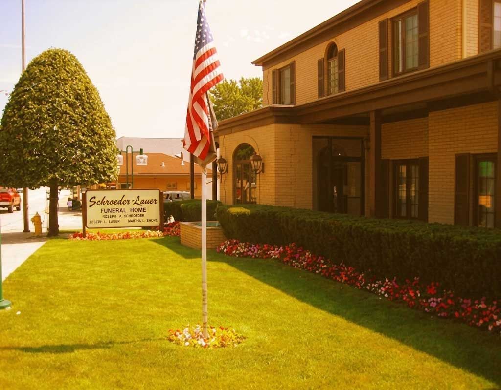 Lawn and flagpole in front of a brown building with a sign and trimmed hedges