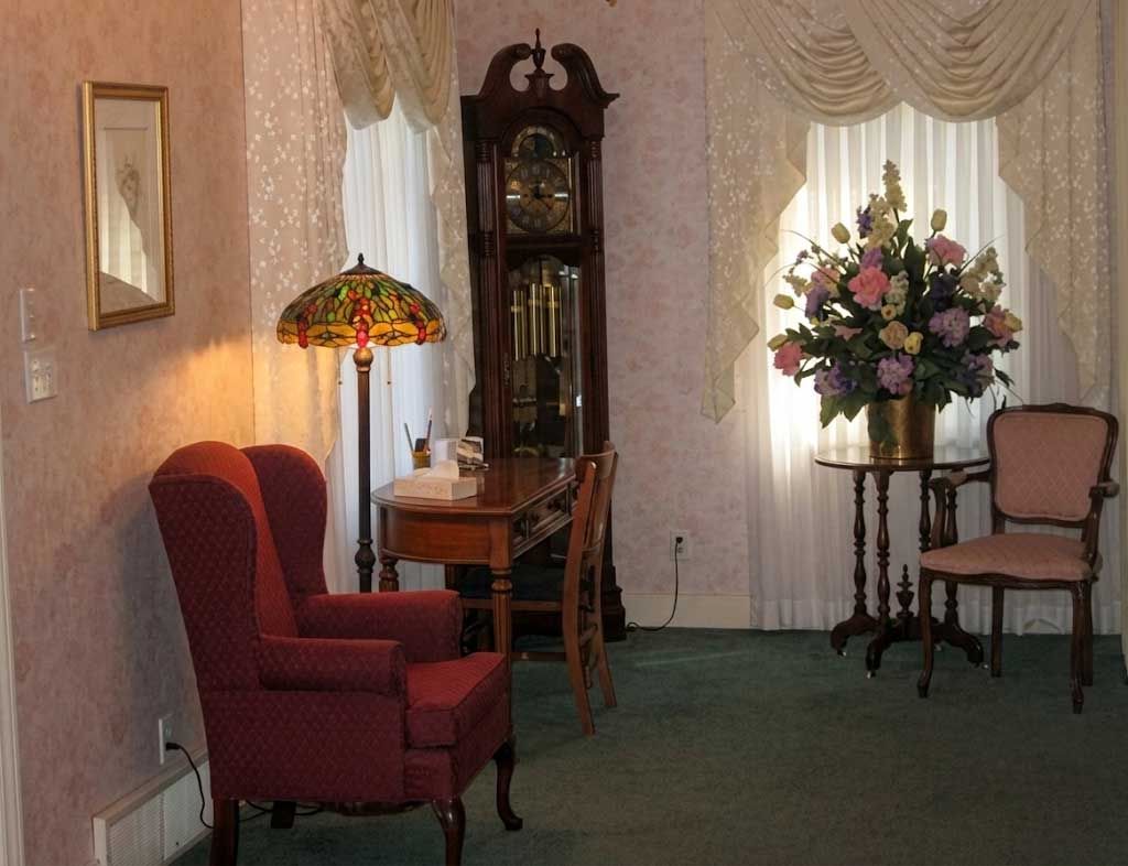 Elegant living room with red armchairs, lamp, floral arrangement, and draped curtains