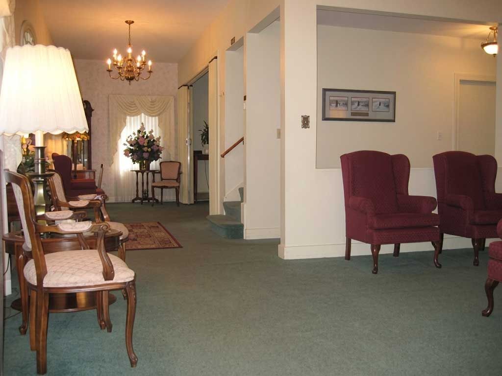 Elegant hallway with green carpet, chandelier, wicker chair, and burgundy armchairs in a well-lit home lobby