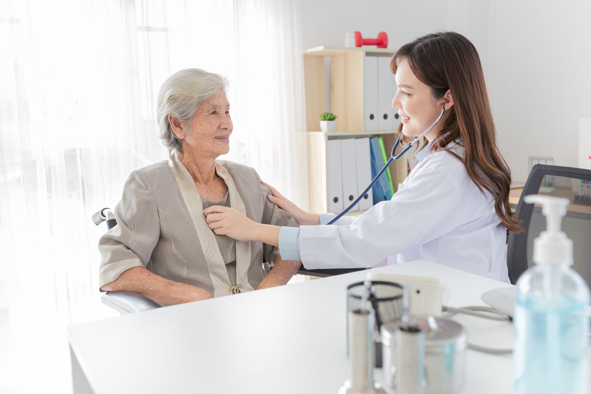 Doctor examining a patient in a bright clinic, listening to her chest with a stethoscope.