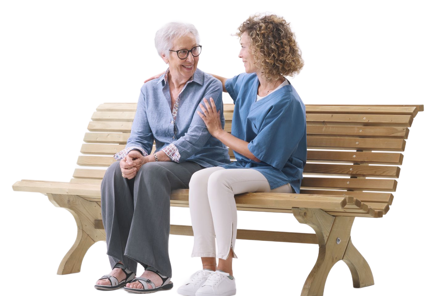 Two women sit on a wooden bench, smiling and talking in a bright, white studio setting.