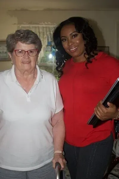 Two women standing indoors, one in a white shirt and one in a red top holding a tablet.