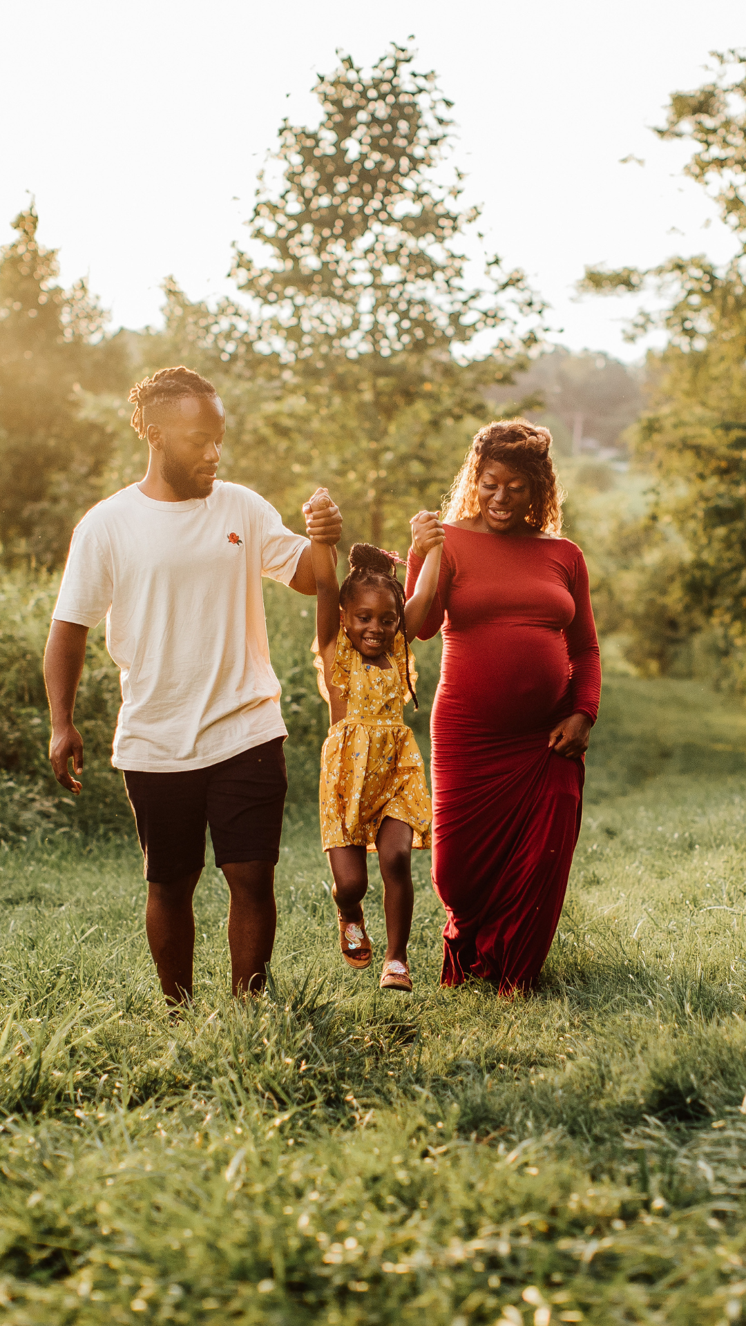 A pregnant woman is walking with her husband and daughter in a park.